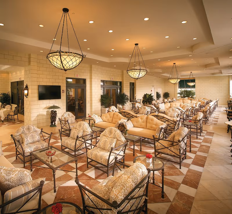 Spacious elegant lounge with rows of cushioned armchairs and sofas under hanging chandeliers.