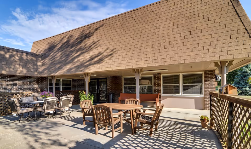 Outdoor covered patio area with wooden and metal tables and chairs in front of a brick building.