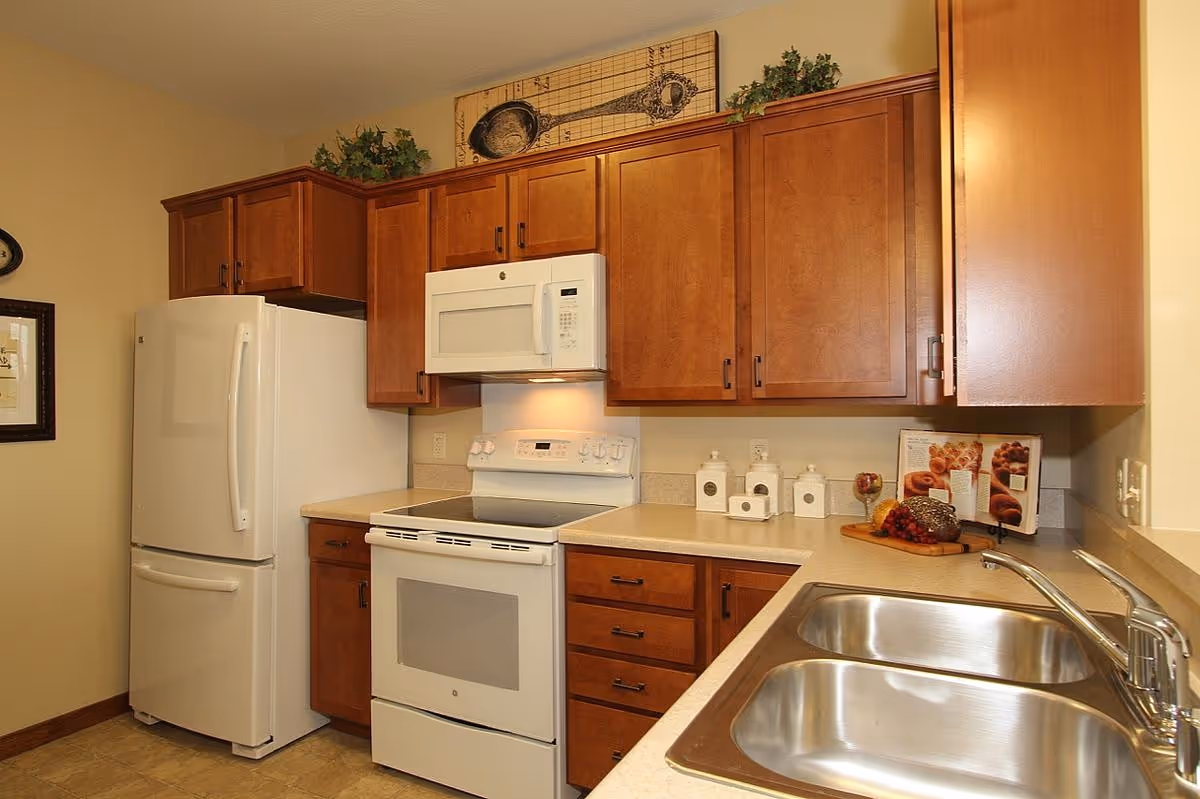 Kitchen with cherry wood cabinets, white refrigerator, stove and microwave, and a double stainless steel sink.