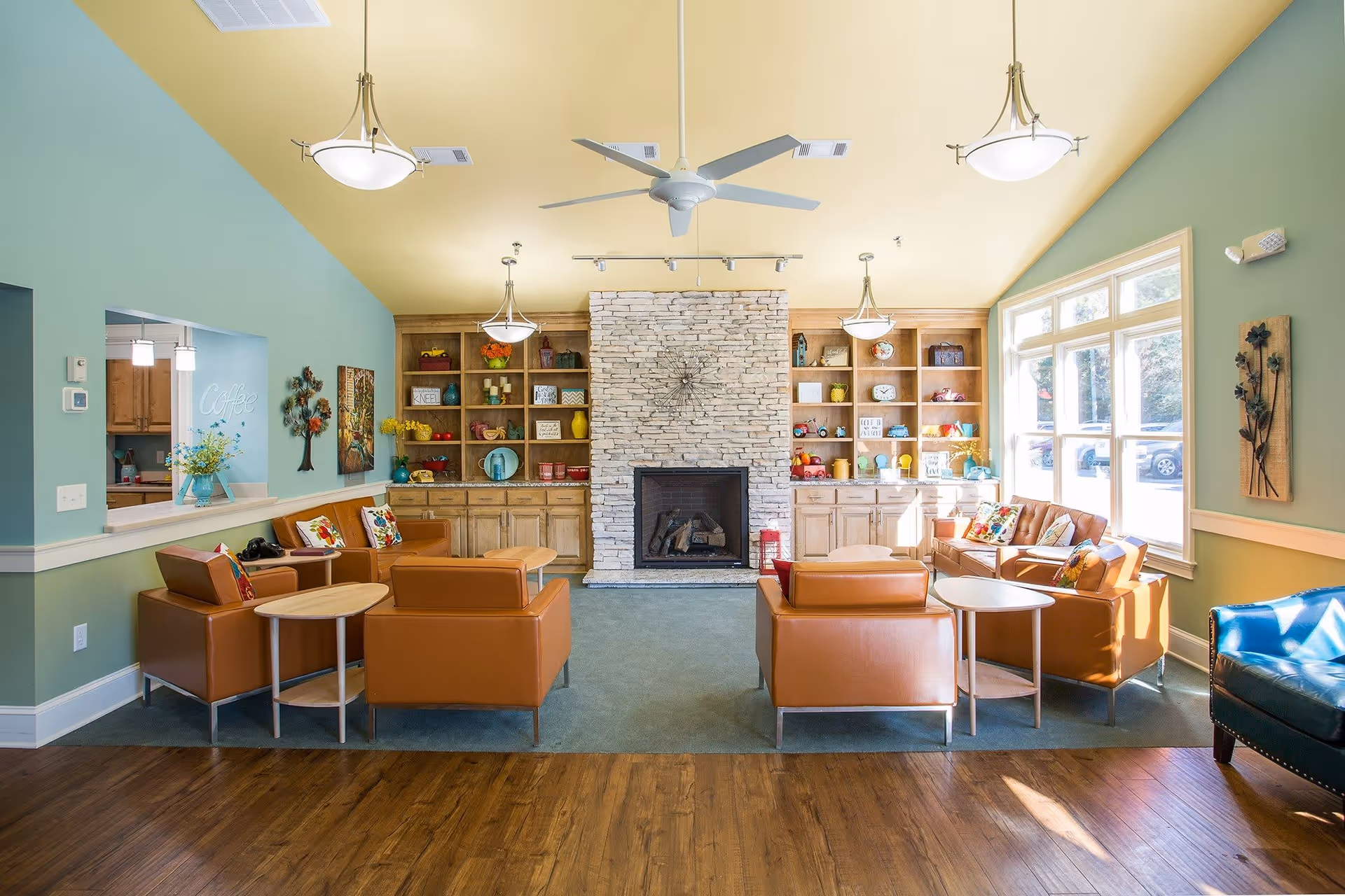 A cozy lobby area featuring comfortable seating, a stone fireplace, and colorful decor. Large windows allow natural light to fill the space, enhancing the inviting atmosphere.