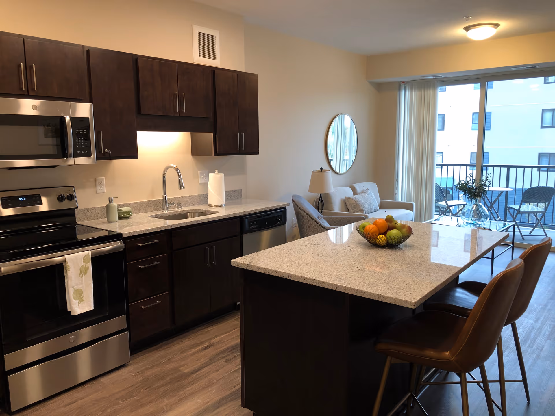 Open modern kitchen with a granite island and bar stools that opens into a living area with a balcony.