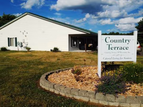 Front exterior of a senior living facility with a sign and landscaped circle.