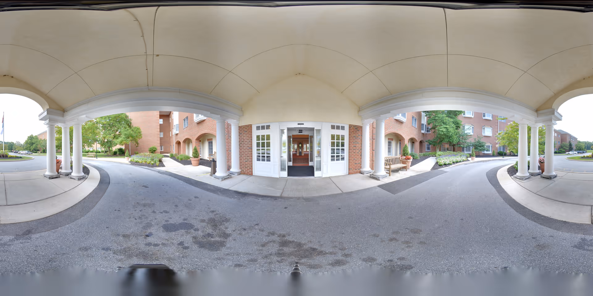 Covered porte-cochere with white columns and double glass doors at the front entrance of a brick senior living building.
