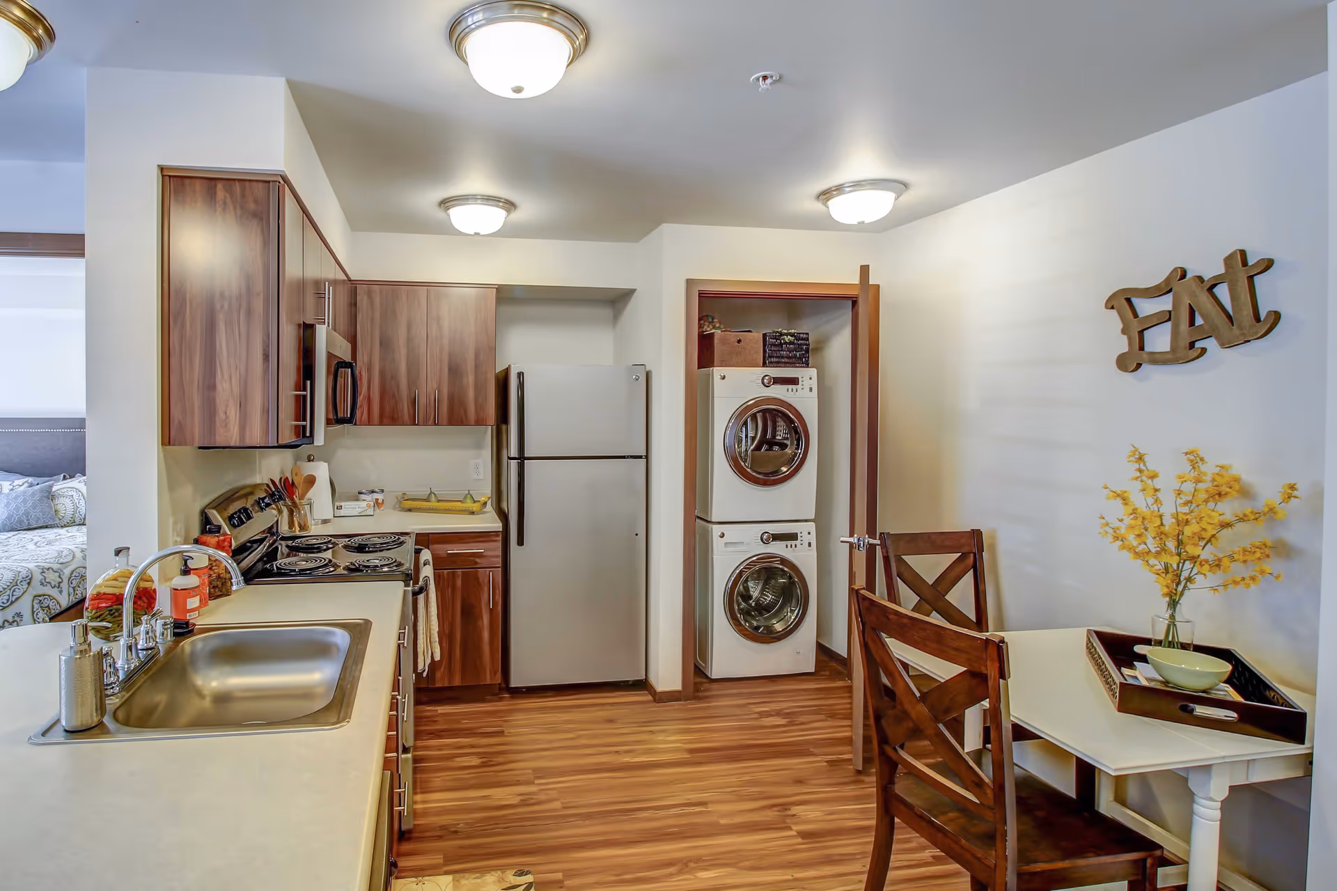Compact kitchen with stainless steel appliances, a stacked washer/dryer in an open closet, and a small dining table with chairs.
