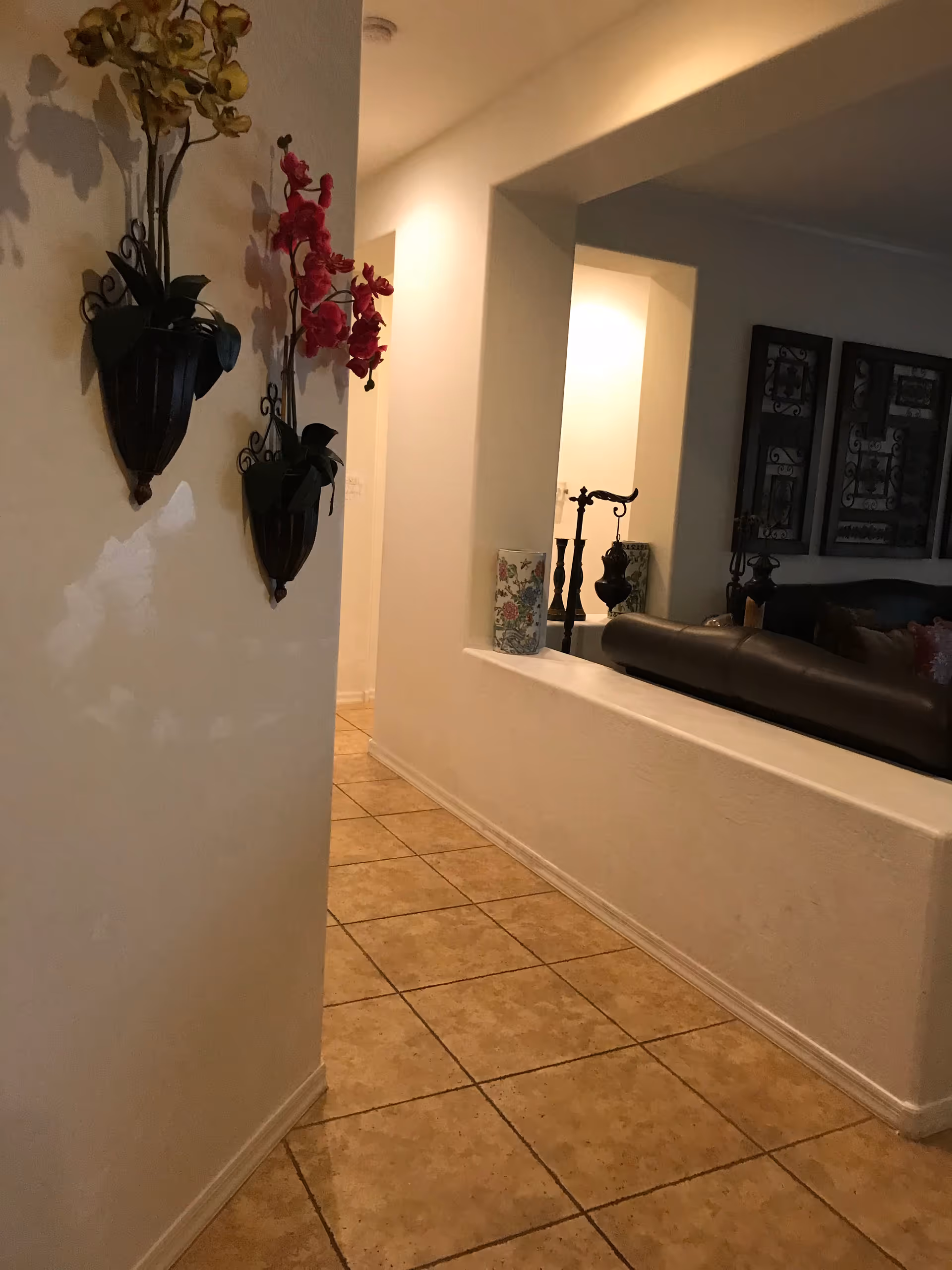 Decorated hallway with tile floor leads to living room with leather sofa and wall art.