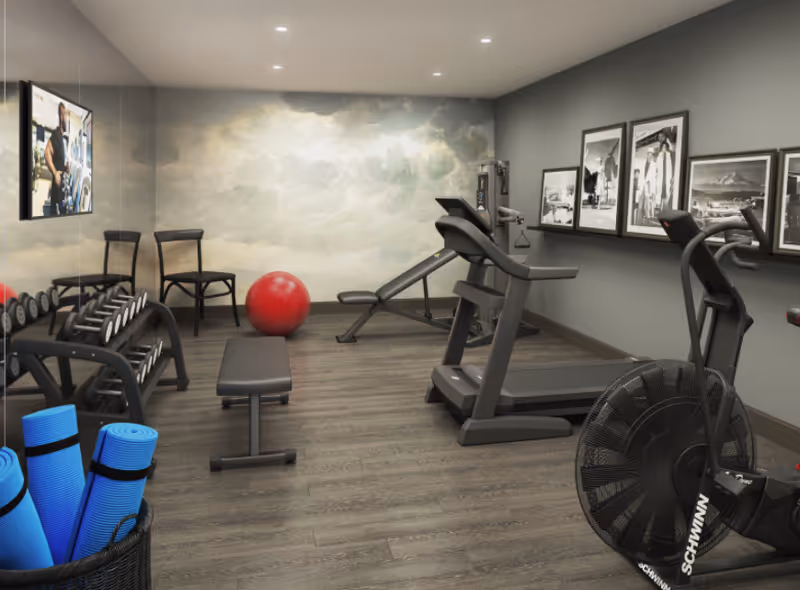 Small fitness room with a treadmill, stationary bike, weight bench and dumbbells, yoga mats, and an exercise ball.