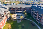 Aerial view of a multi-story senior living complex surrounding a landscaped central courtyard with pathways, seating, and balconies.