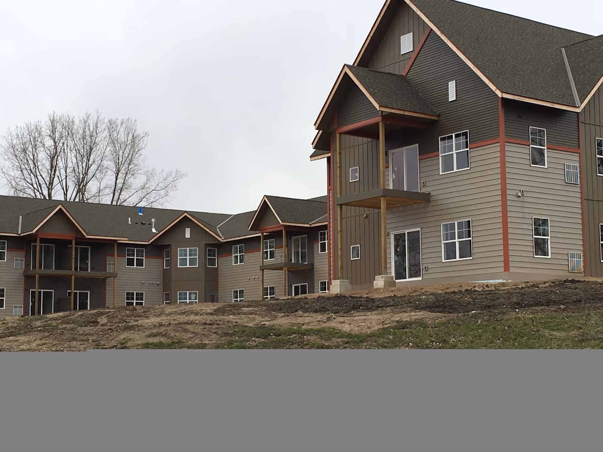 Multi-story gray and brown senior living building with balconies and many windows on a cloudy day.