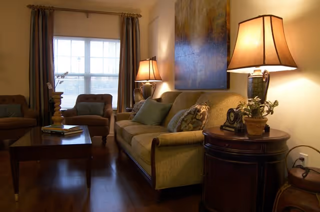 A cozy living room with a sofa, armchairs, coffee table, table lamps, and wall art by a window.