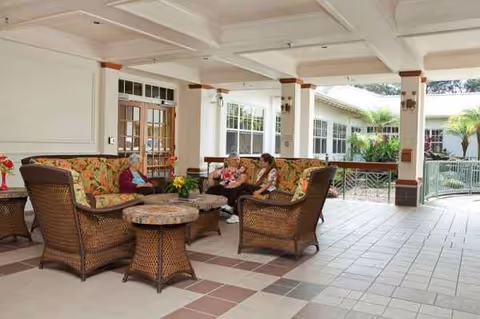 Outdoor shaded seating area with wicker furniture and residents chatting under a covered patio.