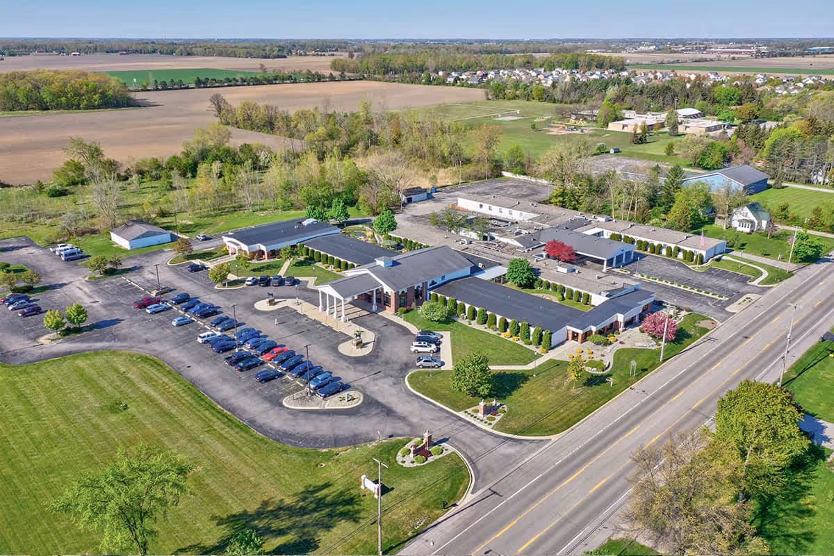 Aerial view of the Carriage House Nursing and Rehab campus showing single-story connected buildings, a parking lot, driveways, and surrounding lawns and fields.