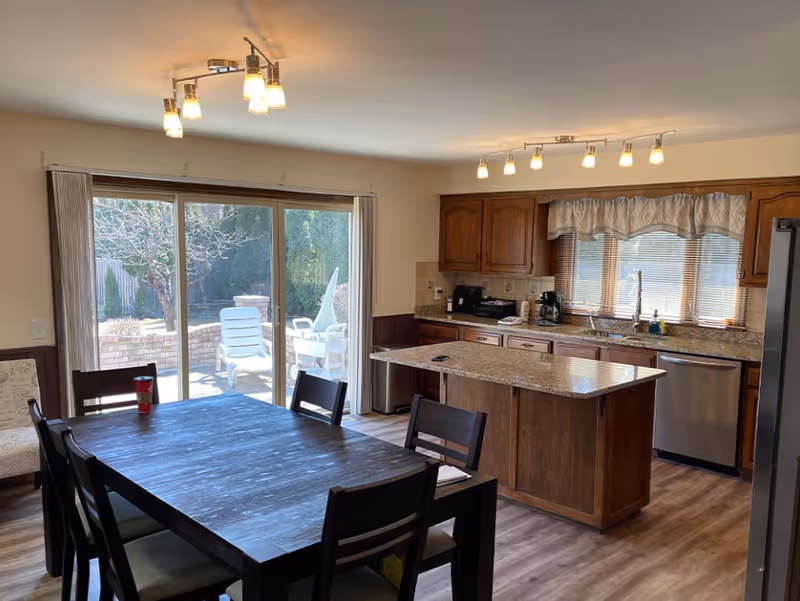 Open-plan kitchen and dining area with a wooden dining table, kitchen island, stainless appliances, and sliding glass doors to a patio.