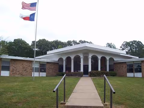 Front view of Caraday of Mineola senior living facility with flagpoles and a walkway.