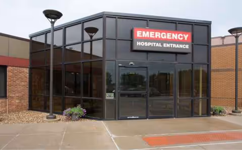 Exterior view of a glass-walled hospital entrance with an Emergency sign.