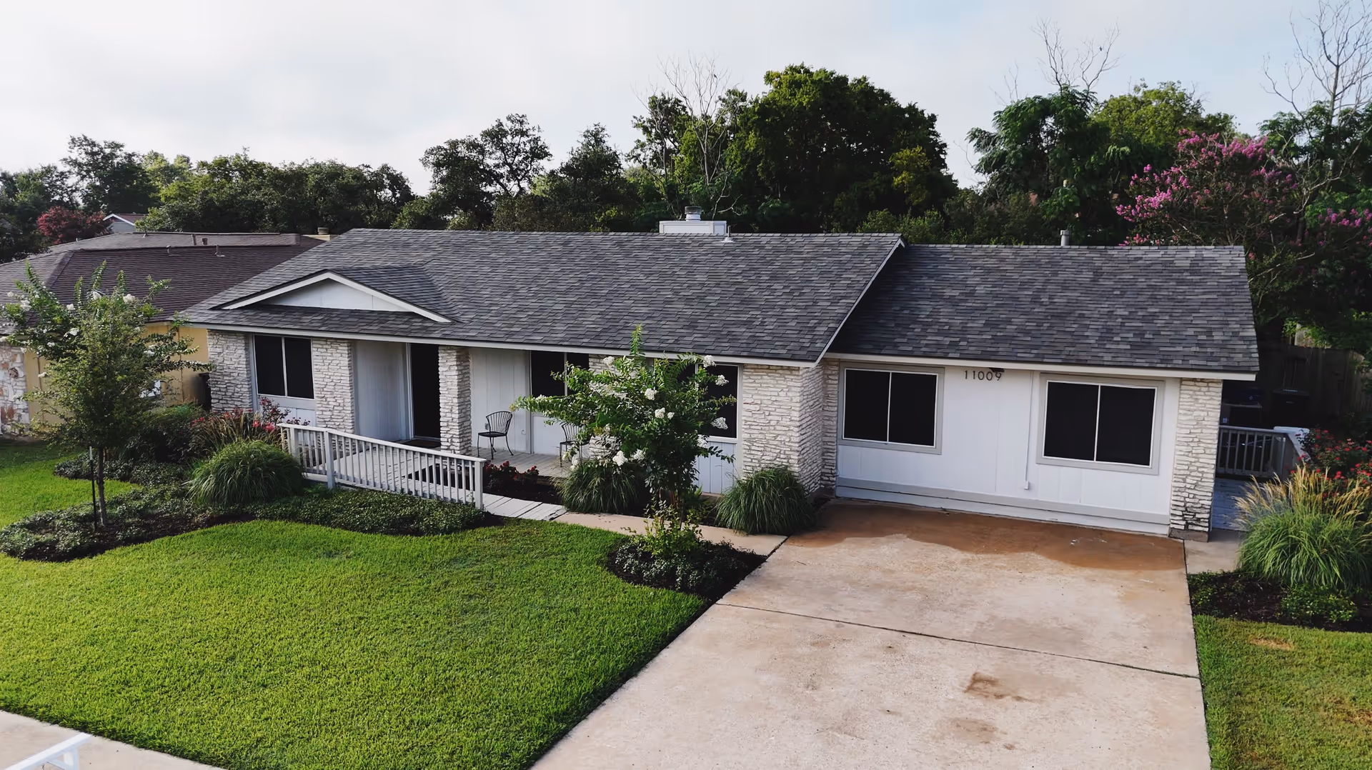 Front exterior of a single-story ranch-style building with a driveway, green lawn, porch ramp, and landscaped yard.