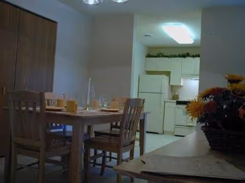 Wood dining table with four chairs set with dishes in a dining area adjacent to a small kitchen.