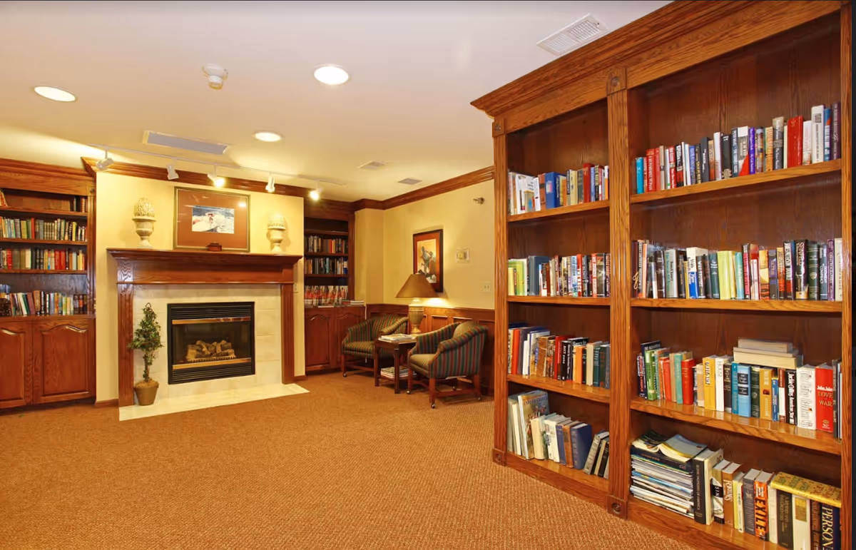 Cozy lounge/library with wooden built-in bookshelves, a fireplace, and armchairs around a small table.