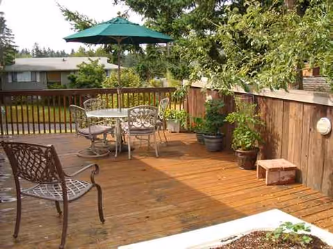 Wooden outdoor deck with metal chairs, a table, umbrella, and potted plants.