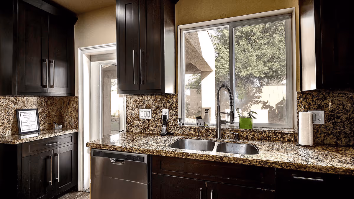 Kitchen with dark wood cabinets, granite countertops, a double sink beneath a window, and a stainless dishwasher.