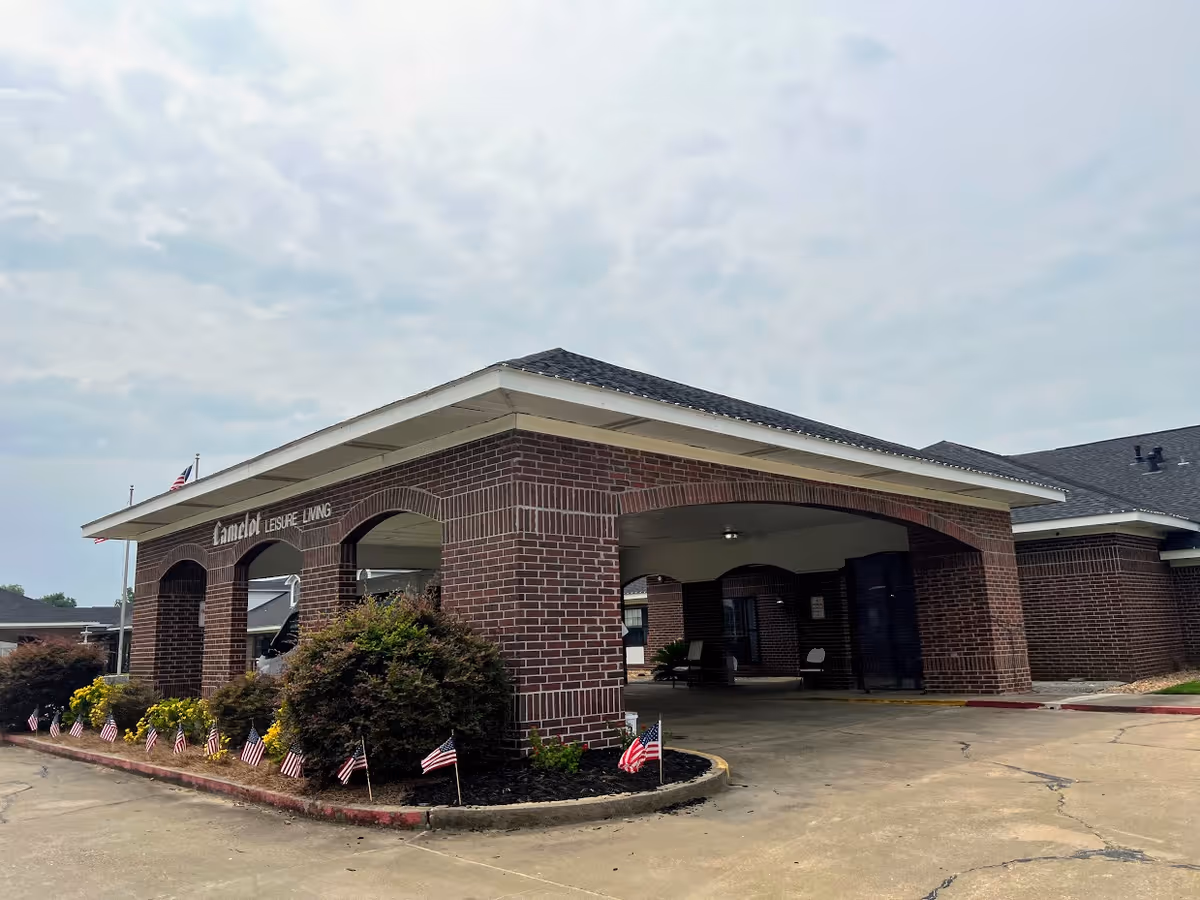 Front brick porte-cochère and entrance of Camelot Leisure Living with small American flags lining the driveway.