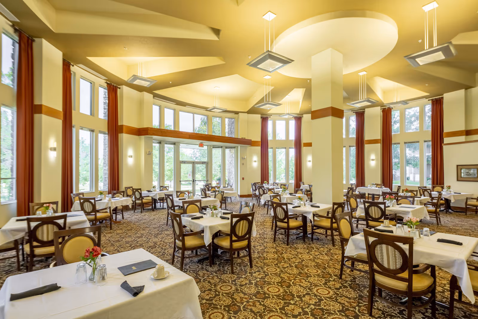 Spacious dining room with multiple set tables and chairs, tall windows, and high decorative ceilings.