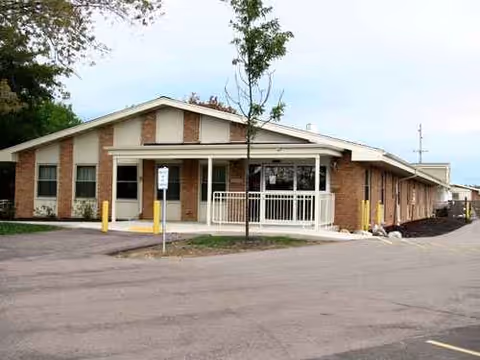 Single-story brick senior living facility exterior with main entrance and parking.