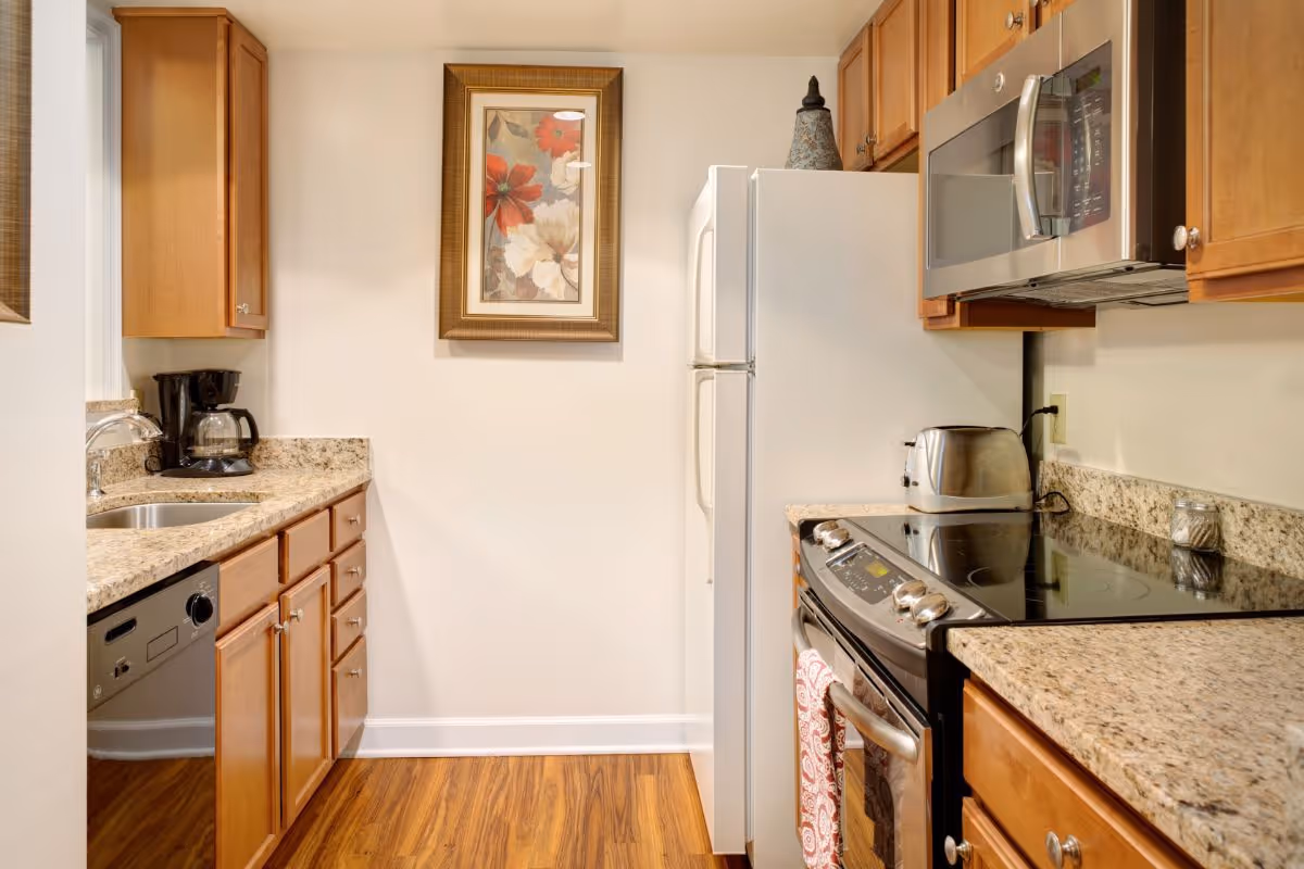 Galley kitchen with wooden cabinets, granite countertops, stainless appliances, and a framed floral print on the wall.