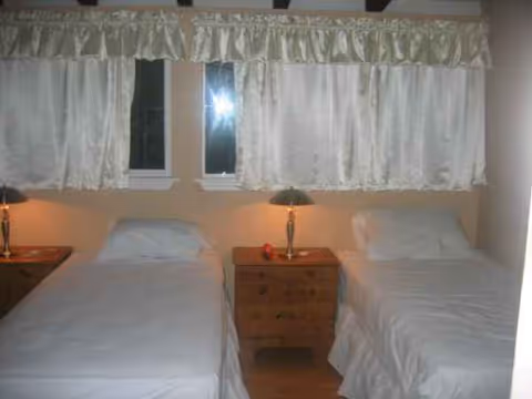 Two single beds with white bedding, nightstands, and curtains in a shared bedroom.