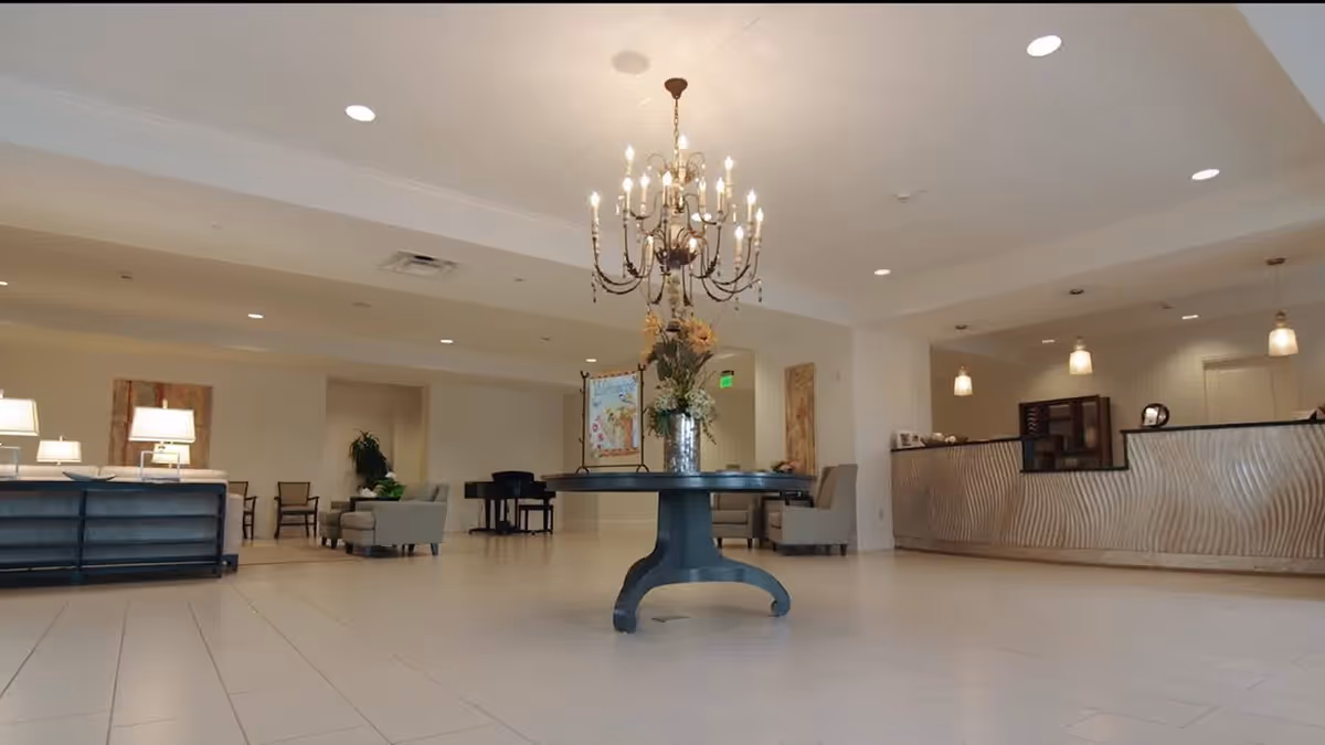 Spacious lobby featuring a central round table with a chandelier overhead, seating areas, and a reception desk in the background.