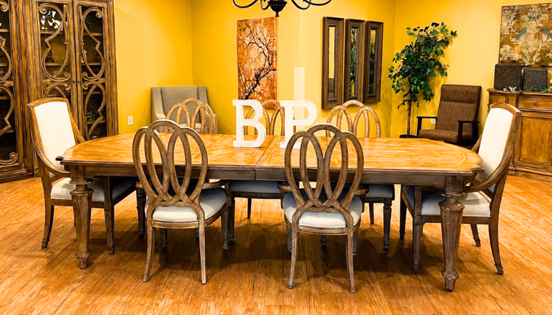 A large wooden dining table surrounded by chairs in a warmly decorated room with yellow walls and artwork.