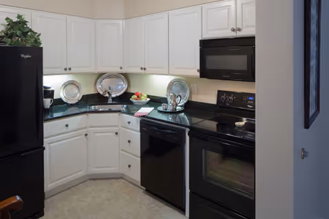 Modern kitchen with white cabinets, black appliances (refrigerator, oven, microwave, dishwasher) and dark granite countertops.