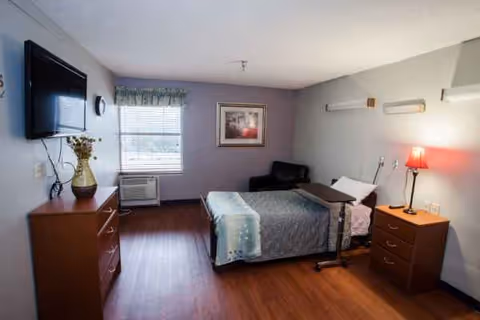 A furnished bedroom with a bed, dresser, nightstands, a wall-mounted TV, and window air conditioner.