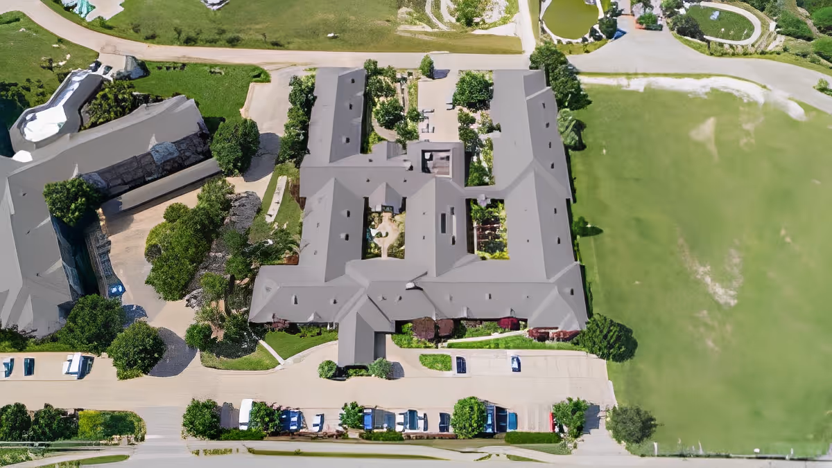 Aerial view of Morada Cedar Hill facility showing multiple buildings with gray roofs, surrounding greenery, parking areas with cars, and pathways.