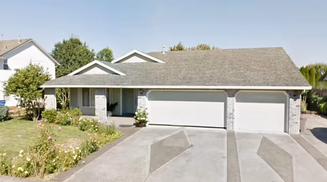 Single-story residential building front with a three-car garage, covered porch and a small lawn with flower beds.