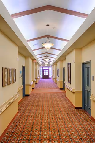 Long corridor inside a senior living facility with patterned carpet and ceiling lights.