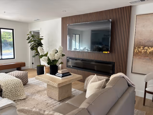 Contemporary living room with a wall-mounted TV above a modern fireplace, a stone coffee table, sofa, and decorative plants.