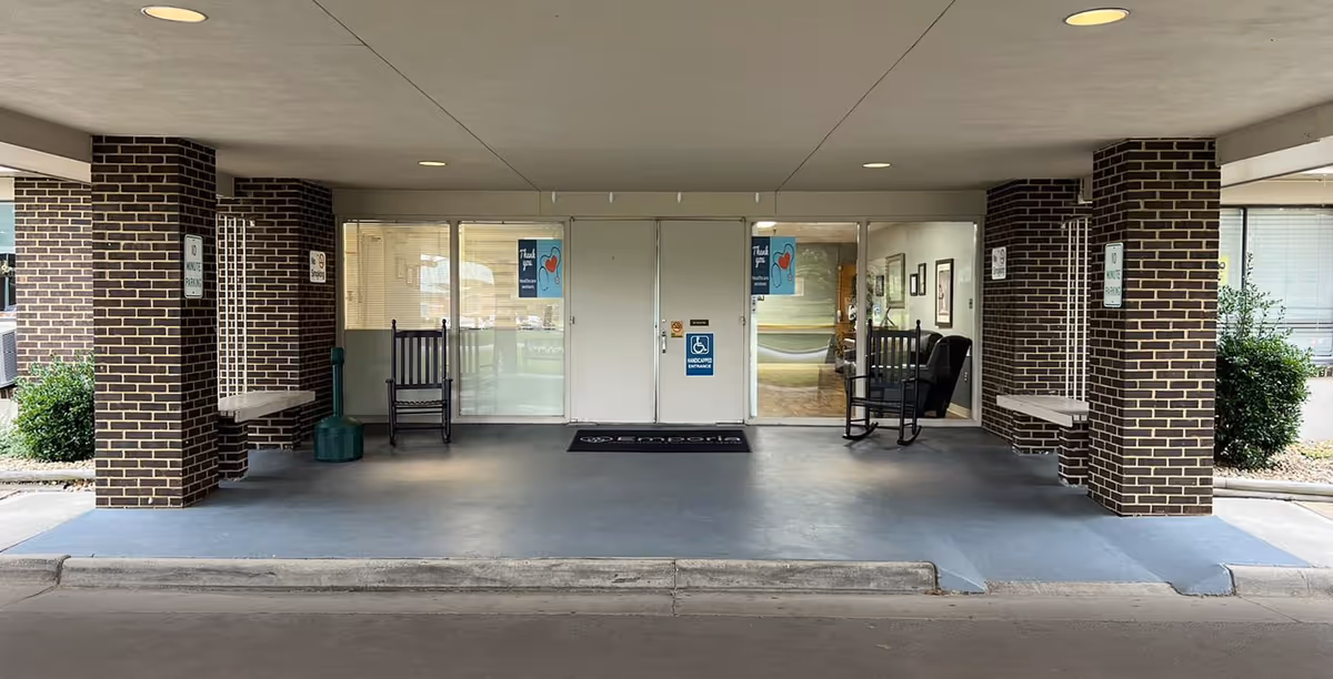 Covered entrance to facility with brick columns, glass doors, benches, and wheelchair-access signage