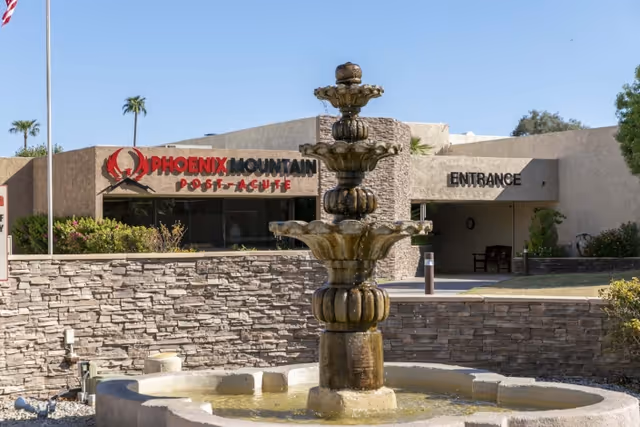 A tiered stone fountain stands in front of the Phoenix Mountain Post-Acute building entrance and signage.