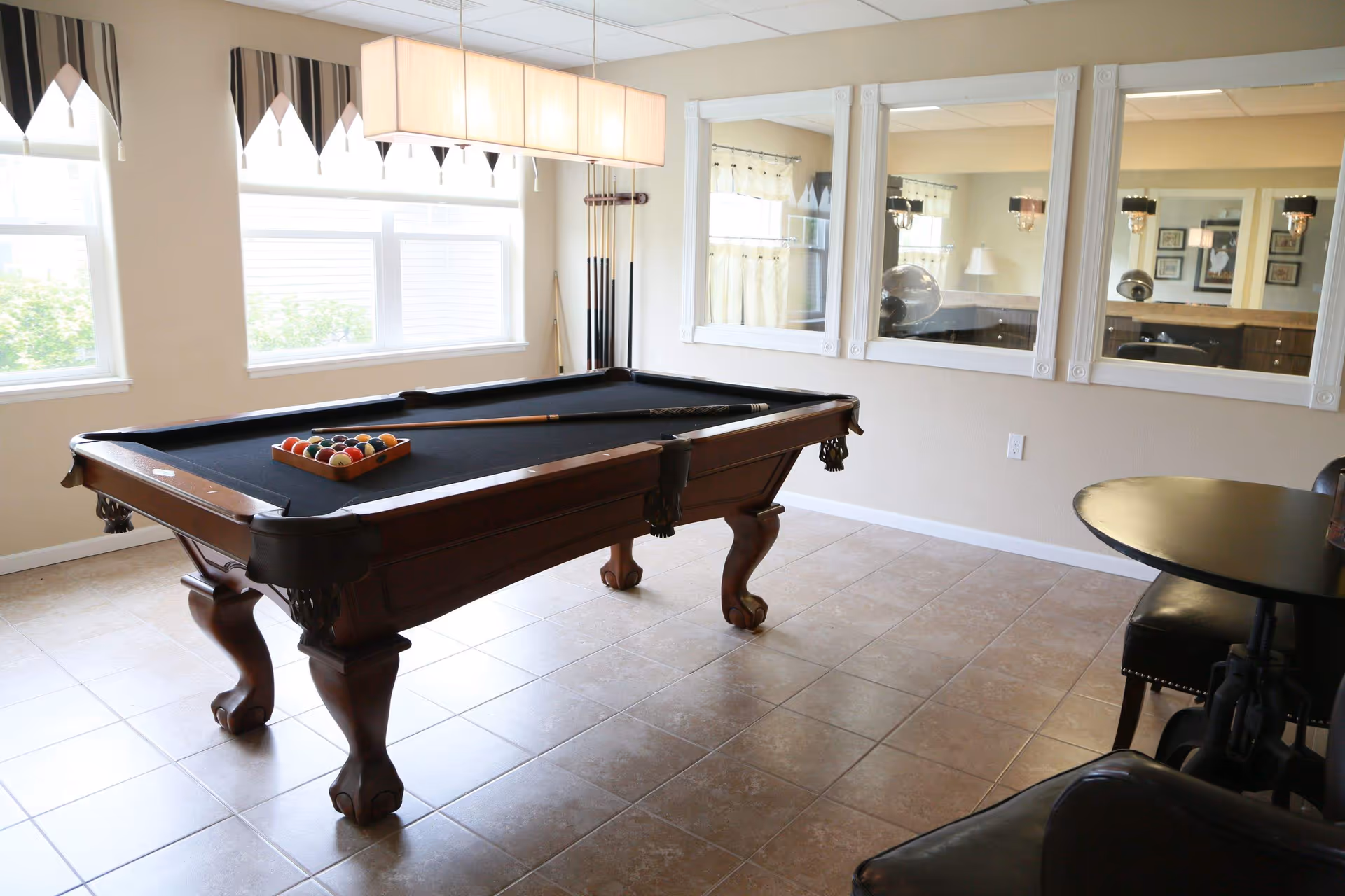 Bright interior room featuring a billiards table with cues, windows, and mirrored wall.