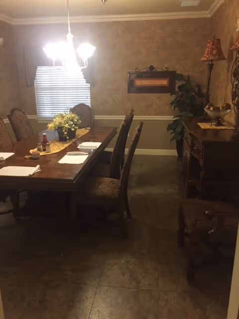 Traditional dining room with a wooden table set with place settings, upholstered chairs, a chandelier, and a sideboard with decor.