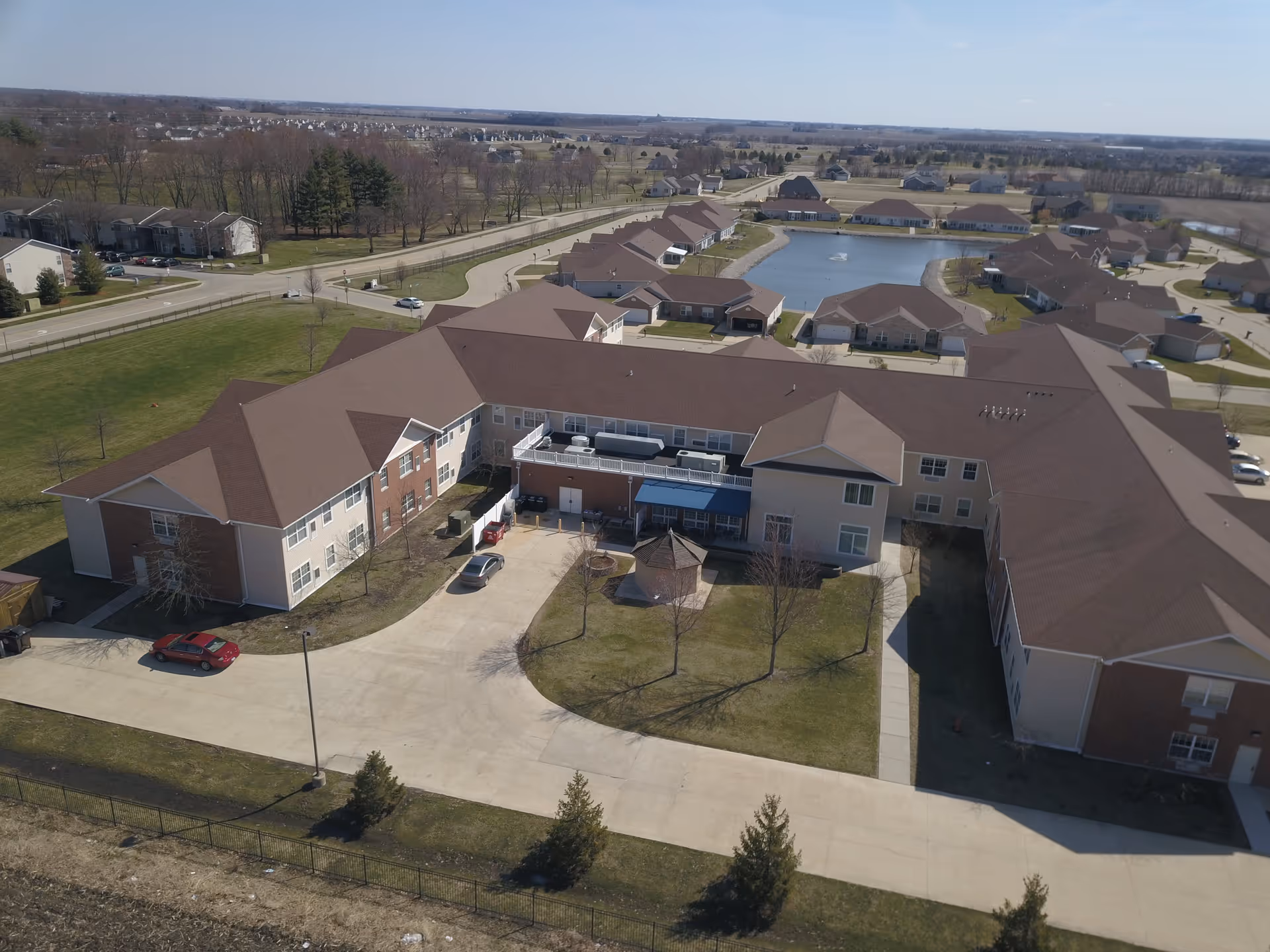 Aerial view of the Prairie Winds of Urbana senior living complex showing interconnected buildings, driveways, lawns and a pond with a fountain.