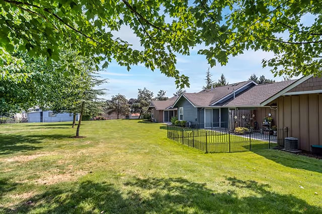 Green lawn and trees beside single-story residential buildings with fenced patios under a blue sky.