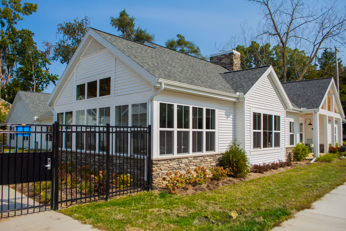 White senior living facility exterior with large windows, stone base, and black gated entrance.