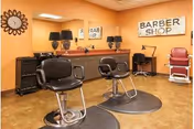 Interior barber shop with two styling chairs, mirrors, lamps, and a red barber chair against an orange wall with a 'BARBER SHOP' sign.