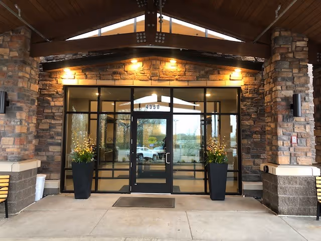 Covered stone-faced building entrance with glass double doors, two large planters, and the address number 4350 above the doors.