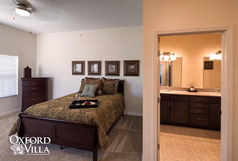Bedroom with a made bed, dresser, and an open doorway revealing a bathroom vanity.