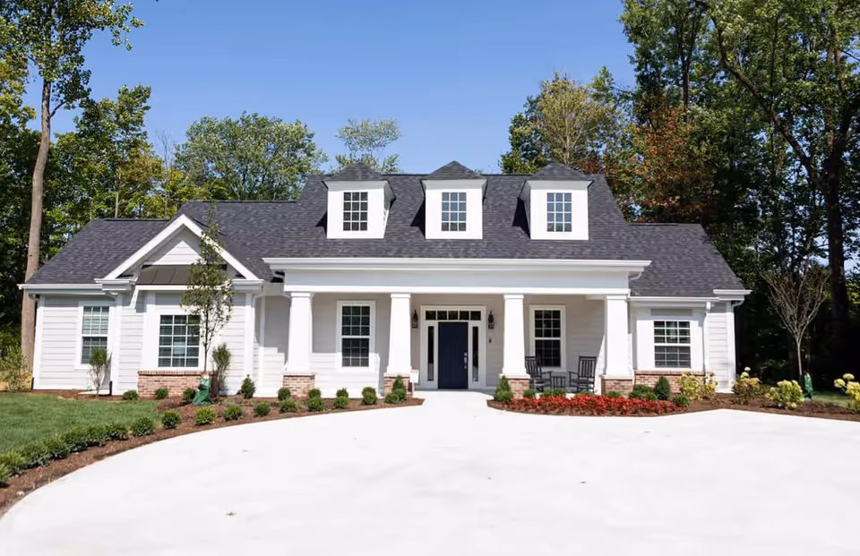 A white cottage-style senior living building with a front porch and circular driveway.