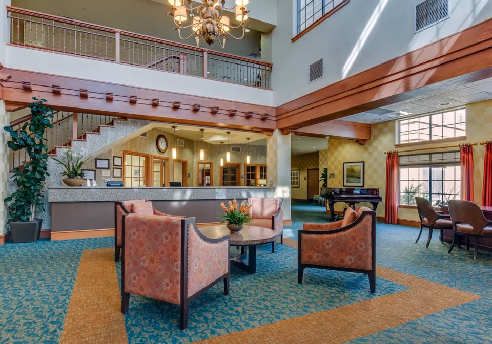 Spacious two-story lobby with a reception desk, seating area, chandelier, piano, and large windows with red curtains.