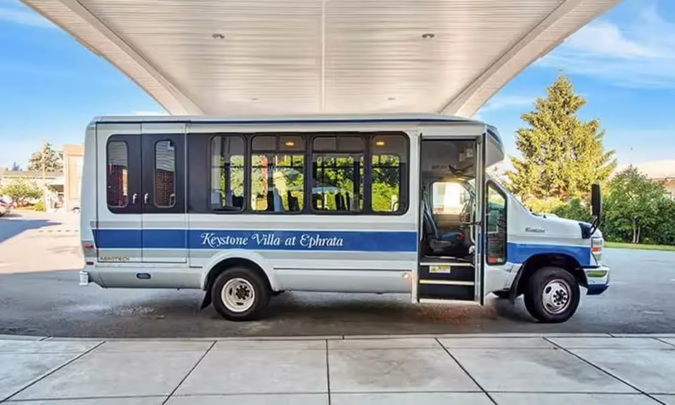 A Keystone Villa at Ephrata shuttle bus parked under a covered drop-off with its door open.