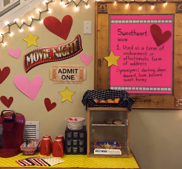 A movie-night themed snack station with a coffee maker, red mugs, pastries and a pink 'Sweetheart' poster on a decorated wall.